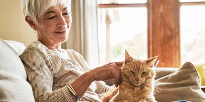 Une femme souriante caresse un chat roux sur ses genoux, sur le canapé.