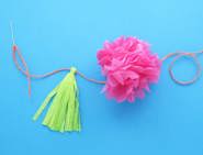 Une fleur en papier essuie-tout rose, et un pompon vert clair attachés ensemble avec une ficelle rouge.