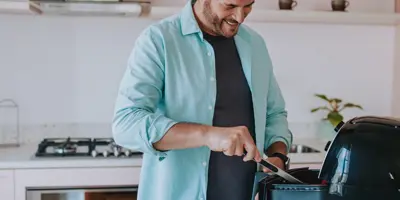 Un homme souriant utilise des pinces pour remuer le contenu d'un air fryer.