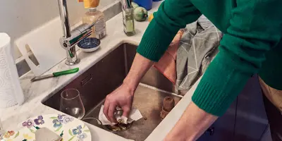 Homme en pull-over vert nettoyant l'évier de la cuisine avec un mouchoir.