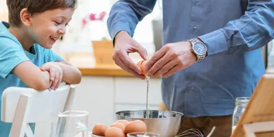 Un homme et un enfant cassent joyeusement des œufs dans un saladier.