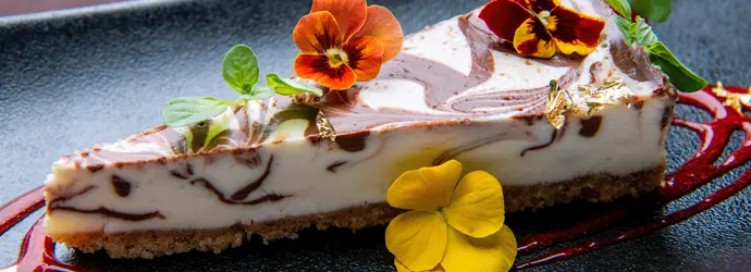 Part de gâteau décorée de fleurs sur une assiette noire. 