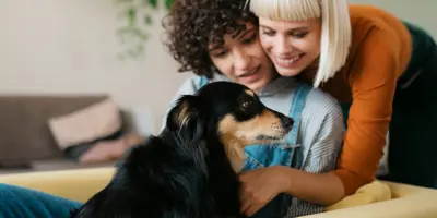 Deux femmes et un chien se blottissent sur un canapé jaune moutarde.