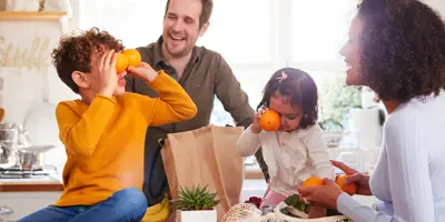 Deux enfants jouent avec des oranges ; des parents déballent leurs courses.