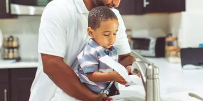 Un père se lave les mains avec son enfant à l'évier de la cuisine.