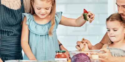 Deux enfants aident joyeusement deux adultes à cuisiner, en mélangeant les ingrédients dans un bol.